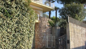 A stone wall with a metal gate, a balcony with railings, and a lush green hedge. - Apartment with garden and wonderful lake view (Bardolino)