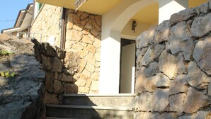 A set of stone steps leading to a building entrance with a stone wall on one side and a yellow awning on the other. - Apartment with garden and wonderful lake view (Bardolino)