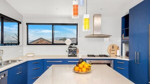 Een moderne keuken met blauwe kastjes, een centraal eiland met fruit, een koffieapparaat en uitzicht op buiten.