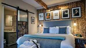 A bedroom with a large bed, a wooden headboard, a nightstand with a lamp, and framed pictures on the wall. - Hare & Hounds Newbury (Newbury)