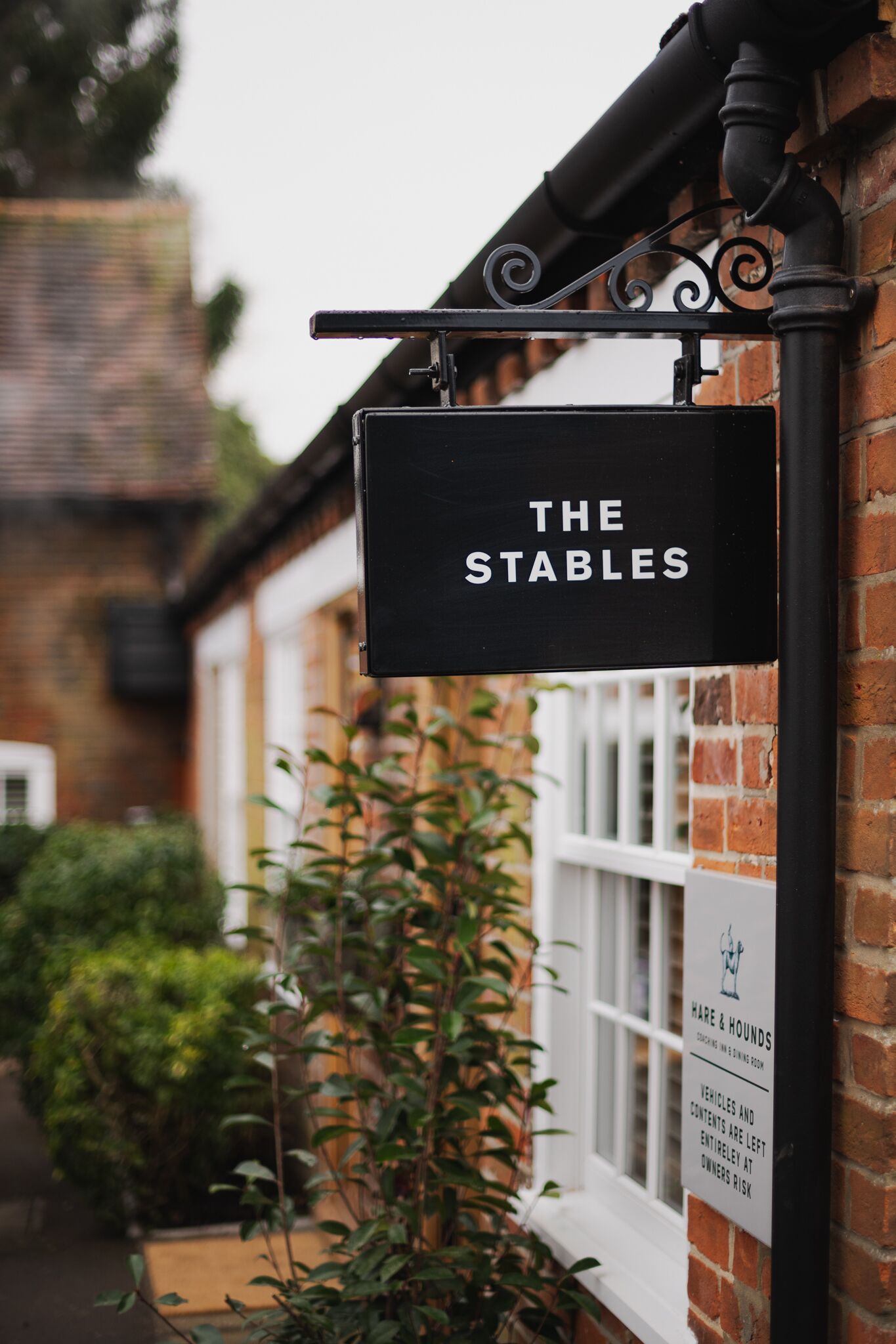 Un letrero negro con letras blancas que dice "THE STABLES" sujeto a una pared de ladrillo.