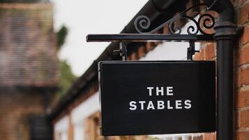 Un letrero negro con letras blancas que dice "THE STABLES" sujeto a una pared de ladrillo.