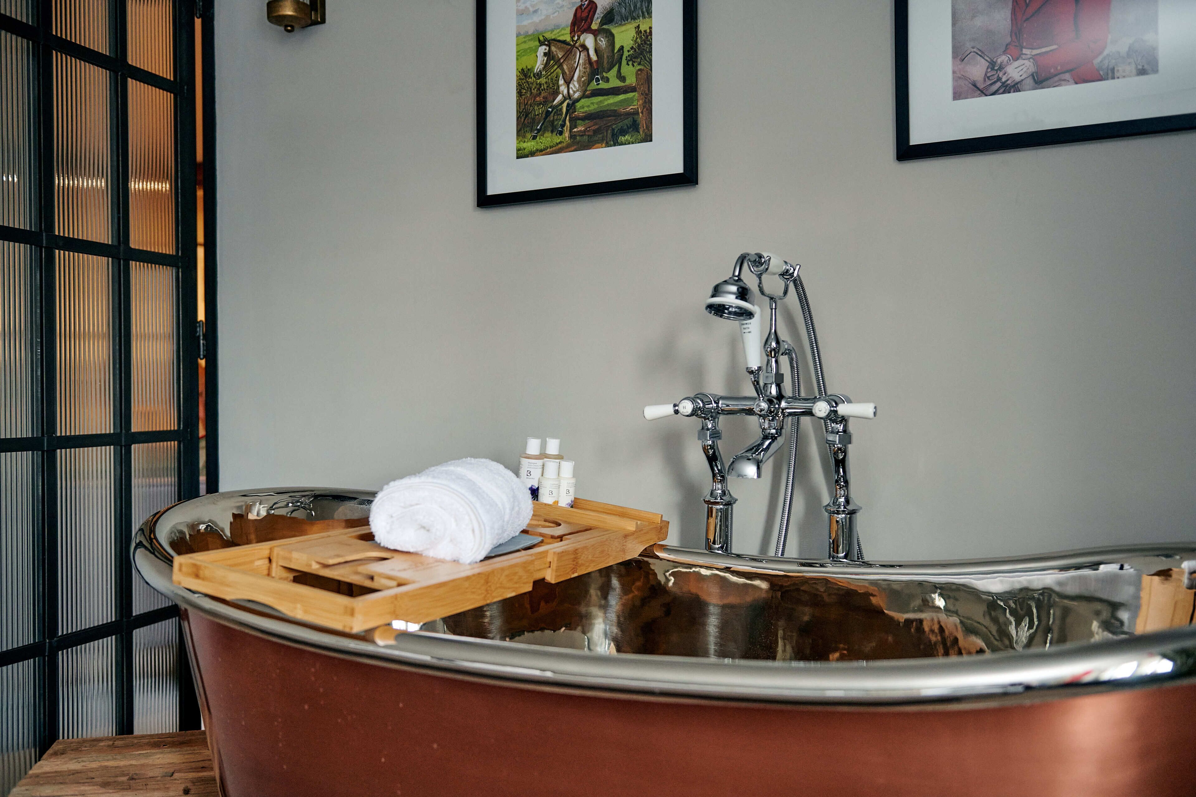 A bathroom with a large copper bathtub, a wooden tray, and a towel.