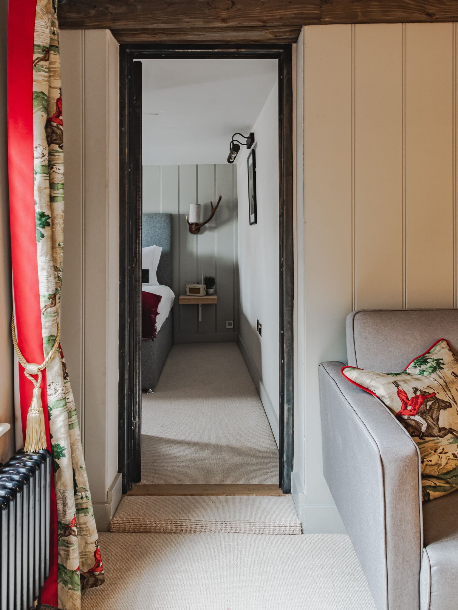 A narrow hallway with a wooden door leading to a room with a bed and a nightstand.