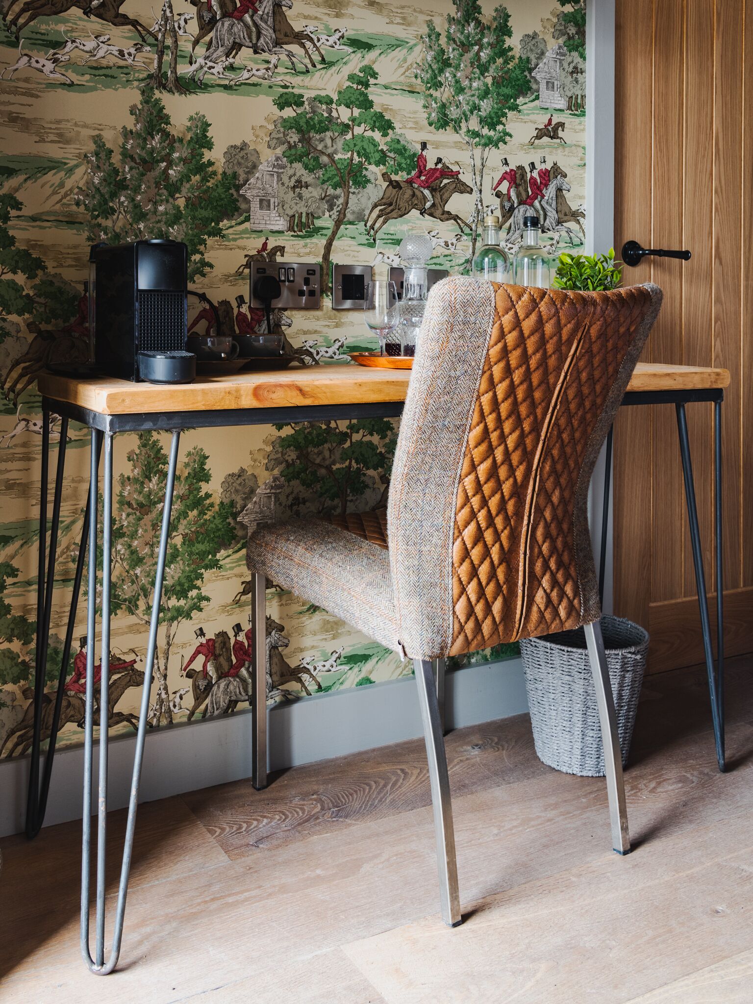 A dining area with a wooden table, a quilted chair, and a wall mural.
