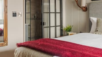 Un dormitorio moderno con una cama grande, una puerta corrediza de vidrio que da a una ducha, una lámpara en forma de cabeza de venado montada en la pared y un cuadro enmarcado.
