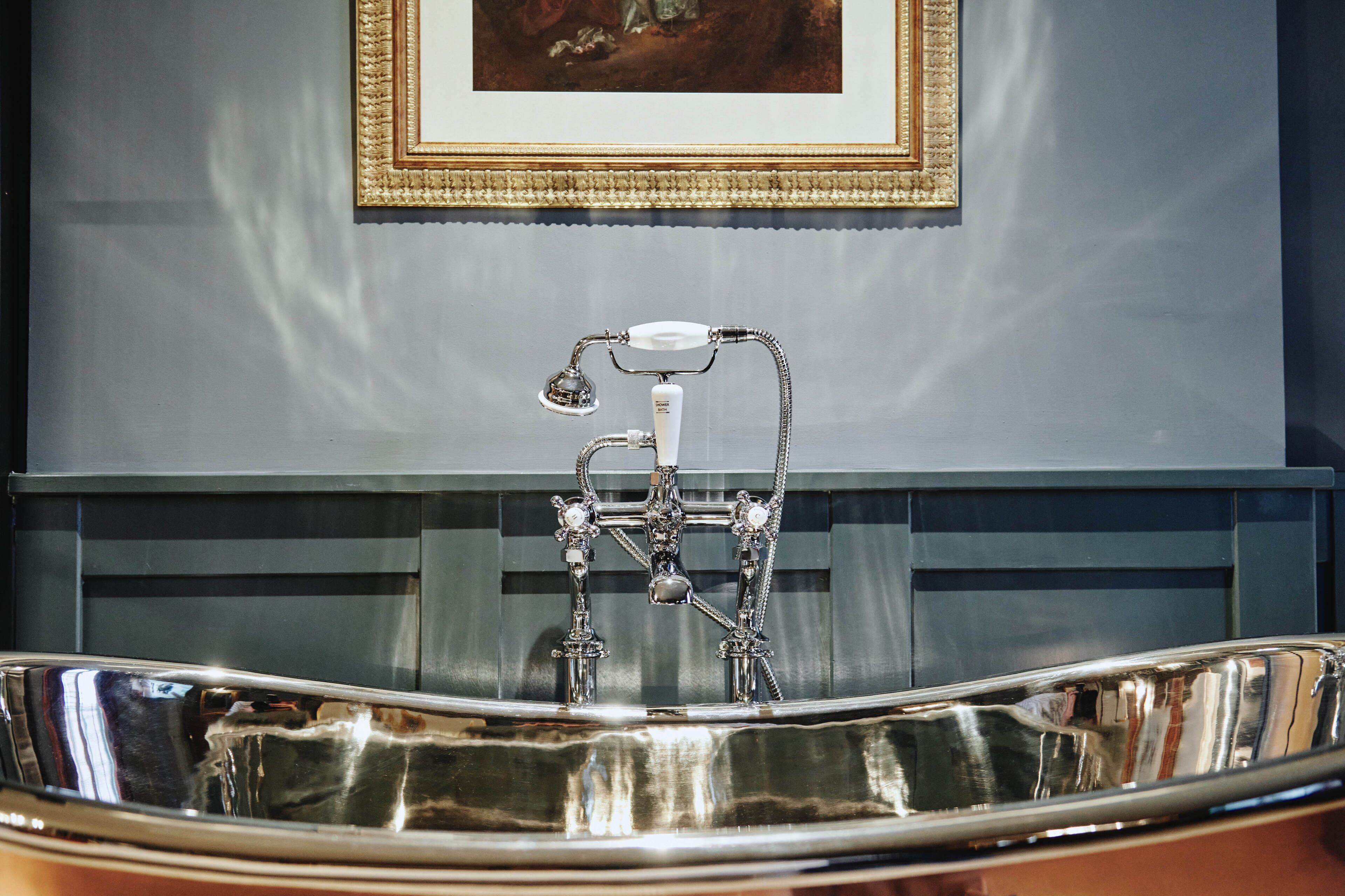 A bathroom with a large, ornate bathtub, a framed painting on the wall, and a dark-colored vanity.