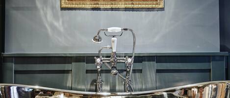 A bathroom with a large, ornate bathtub, a framed painting on the wall, and a dark-colored vanity.