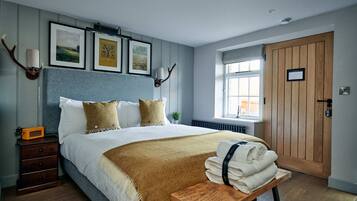 A bedroom with a large bed, a wooden nightstand, a bedside table with towels, a window with a view, and wall-mounted artwork.