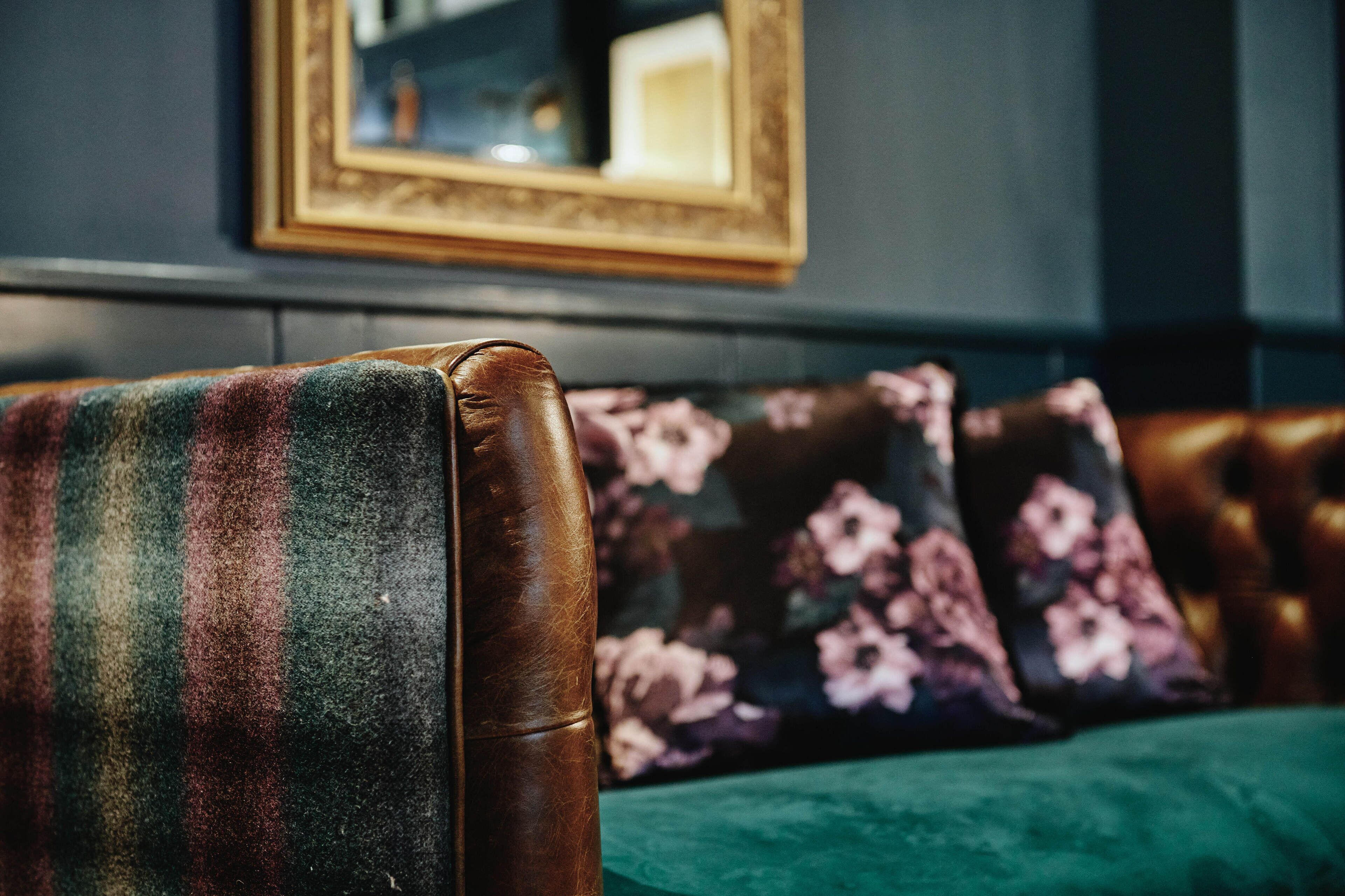 A leather armchair with a colorful blanket, a floral pillow, and a green cushion.