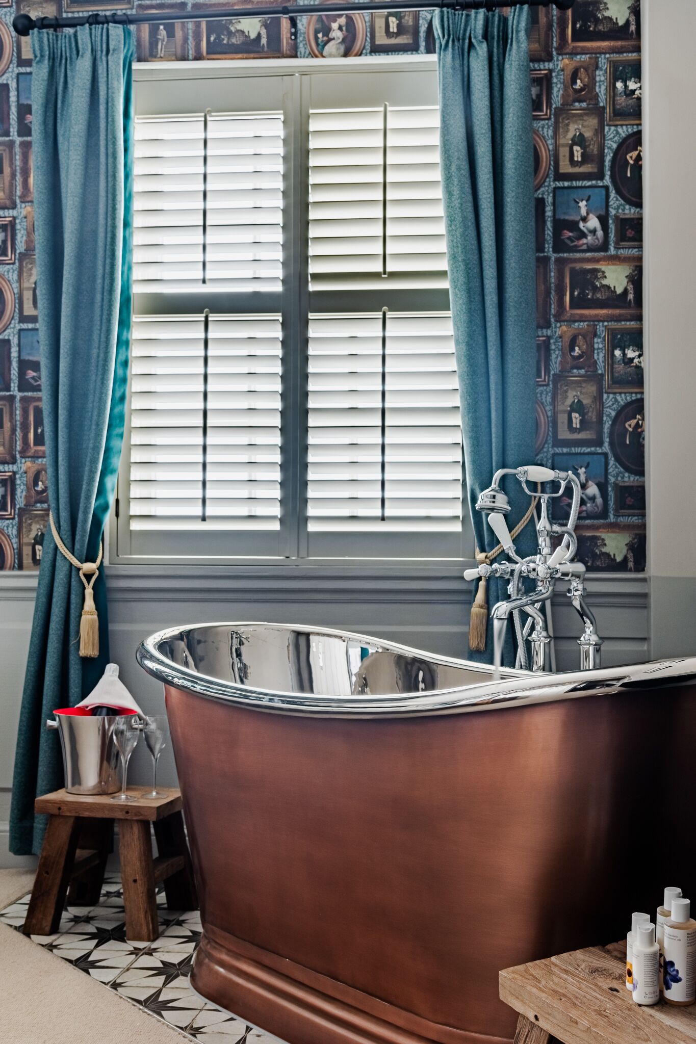 Un baño con una bañera independiente, una ventana con persianas y un papel tapiz estampado.