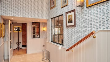Un pasillo con papel tapiz estampado, obras de arte enmarcadas y una escalera de madera.