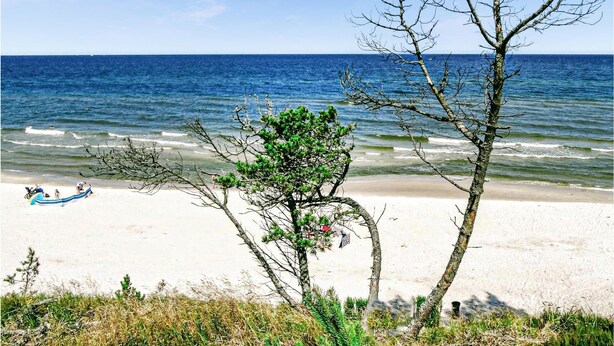 Ein Strand mit freiem Blick auf das Meer, einige Personen und ein kleines Boot im Sand.