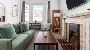 Un salon avec un canapé vert, une table basse en bois, une cheminée et une grande fenêtre avec des rideaux.