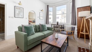 Un salon moderne avec un canapé vert, une table basse en bois et une vue sur la ville grâce à de grandes fenêtres.