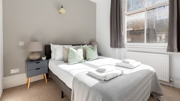 Une chambre à coucher avec un lit, une table de chevet, une lampe et une fenêtre avec des rideaux.