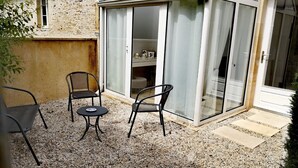 A patio area with a glass door leading to a room, two chairs, a small table, and a gravel floor. - Cosy apartment in the heart of Bayeux (Bayeux)