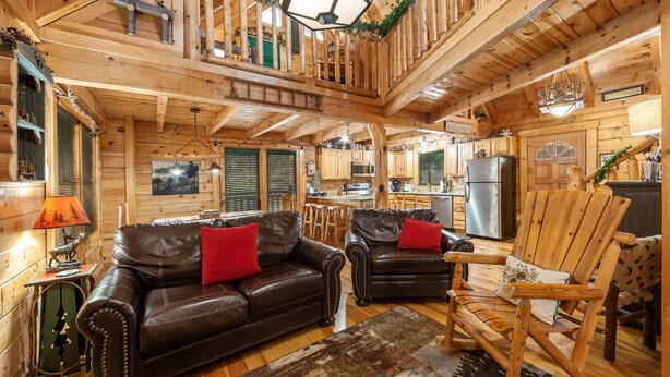 A wooden cabin interior with a living room featuring two leather sofas, a wooden rocking chair, and a kitchen area with modern appliances. - 3 BR w/ Hot Tub, WiFi, Pool Access, Close to Town, Free Attraction Tickets Daily (Pigeon Forge)