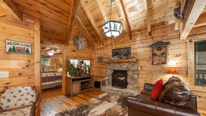 A cabin interior with a stone fireplace, wooden walls, a clock, and a welcome sign. - 3 BR w/ Hot Tub, WiFi, Pool Access, Close to Town, Free Attraction Tickets Daily (Pigeon Forge)