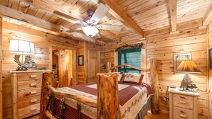 A log cabin bedroom with a wooden bed, a dresser, a nightstand, and a ceiling fan. - 3 BR w/ Hot Tub, WiFi, Pool Access, Close to Town, Free Attraction Tickets Daily (Pigeon Forge)
