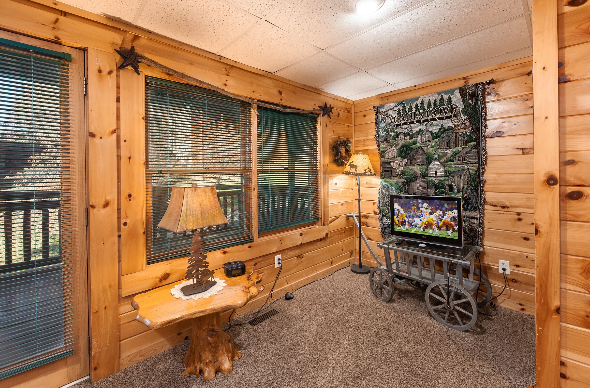 L’intérieur chaleureux d’un chalet avec des murs en bois, un banc en bois, une lampe, un téléviseur posé sur un chariot et une fresque représentant un paysage rural.