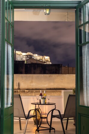 An open balcony with two chairs, a table with bottles and glasses, and a view of a building under a dark sky.