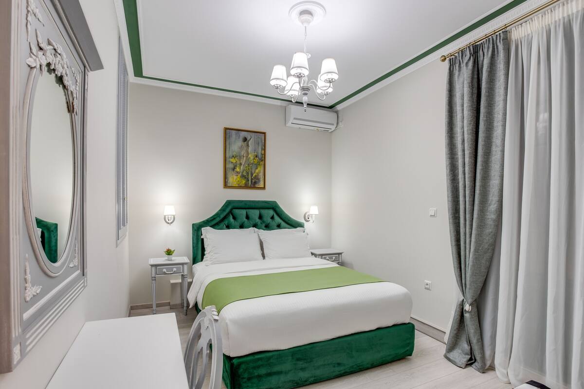 A neatly arranged bedroom with a bed, bedside tables, a mirror, and a painting on the wall.
