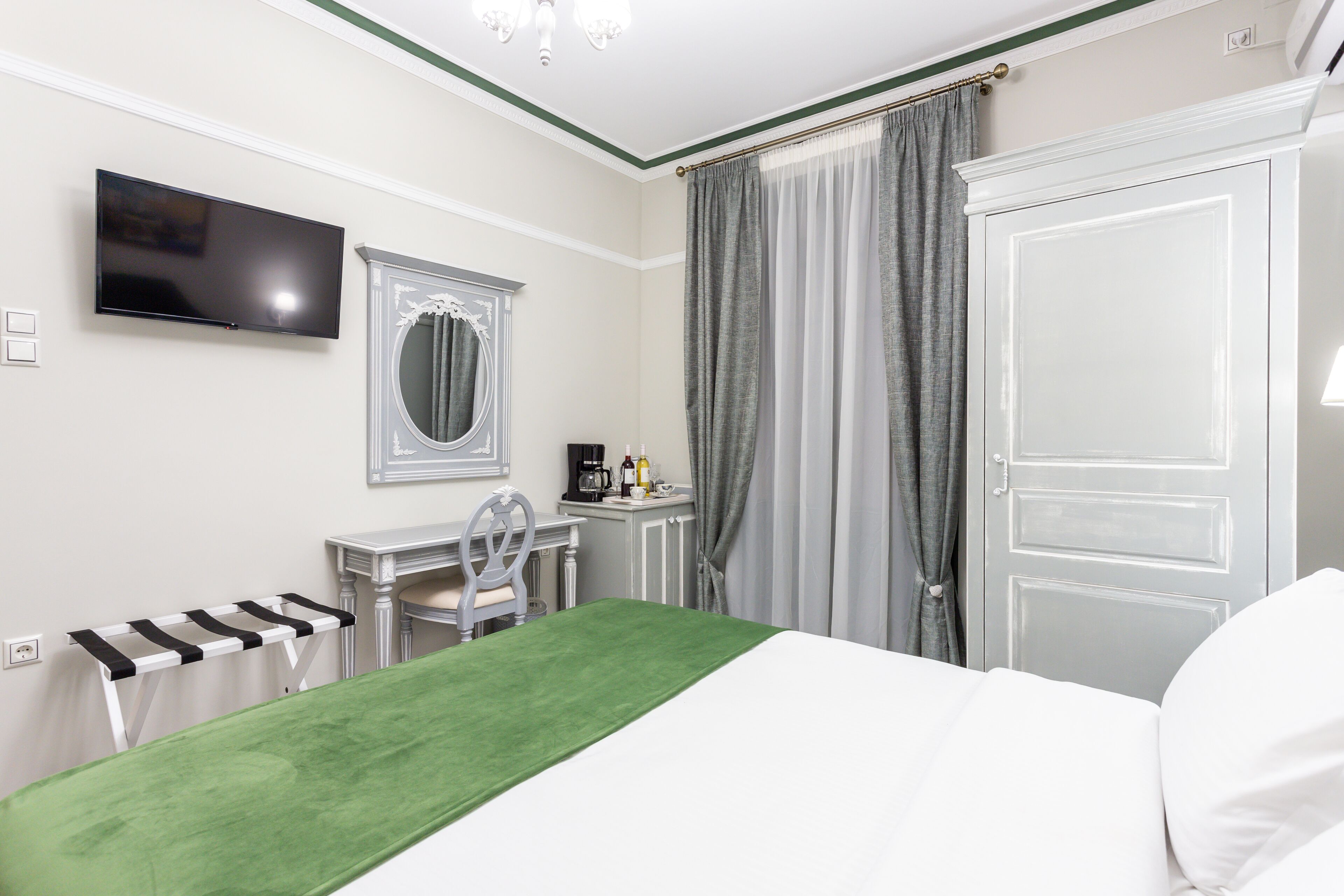 Quarto de hotel com cama, escrivaninha, cadeira, televisão, espelho e porta.