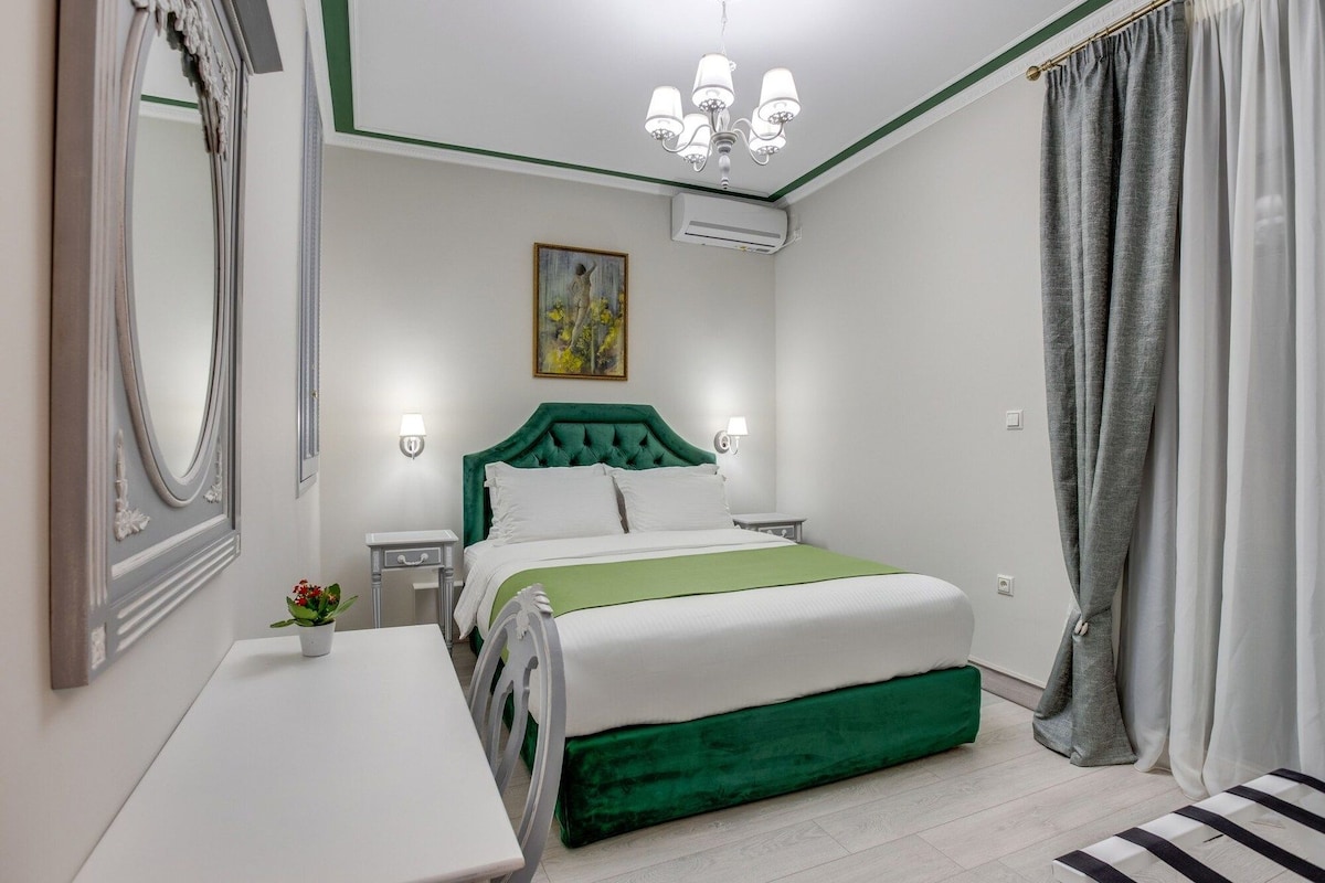 A hotel room with a bed, bedside tables, a mirror, a painting, and a chandelier.