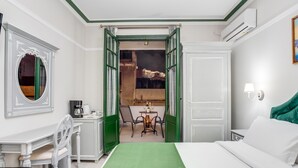 Une chambre d’hôtel avec une couvre-lit verte, un bureau avec une chaise, une table à manger avec des chaises et une vue sur le balcon extérieur.