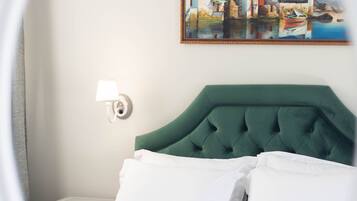 A hotel room with a green upholstered headboard, white bedding, a painting of a coastal scene, and a bedside lamp.