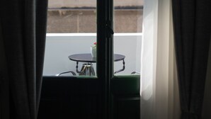 Une fenêtre avec des rideaux, une vue sur un bâtiment à l’extérieur et une table avec une chaise à l’intérieur.