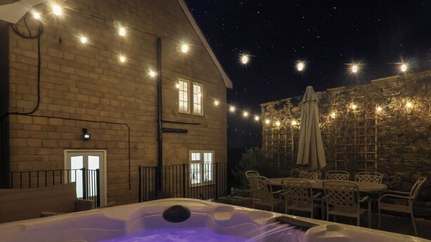 Una vasca idromassaggio con illuminazione viola, circondata da mobili da esterno e luci decorative.