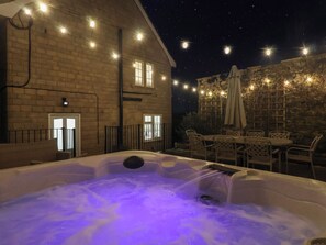 Un bain à remous éclairé d’une lumière violette, entouré de meubles d’extérieur et de guirlandes lumineuses.