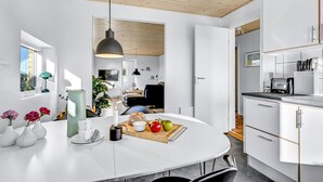 Een moderne keuken met witte kasten, een centraal eiland met een schaal fruit, en een eethoek met een tafel en stoelen.