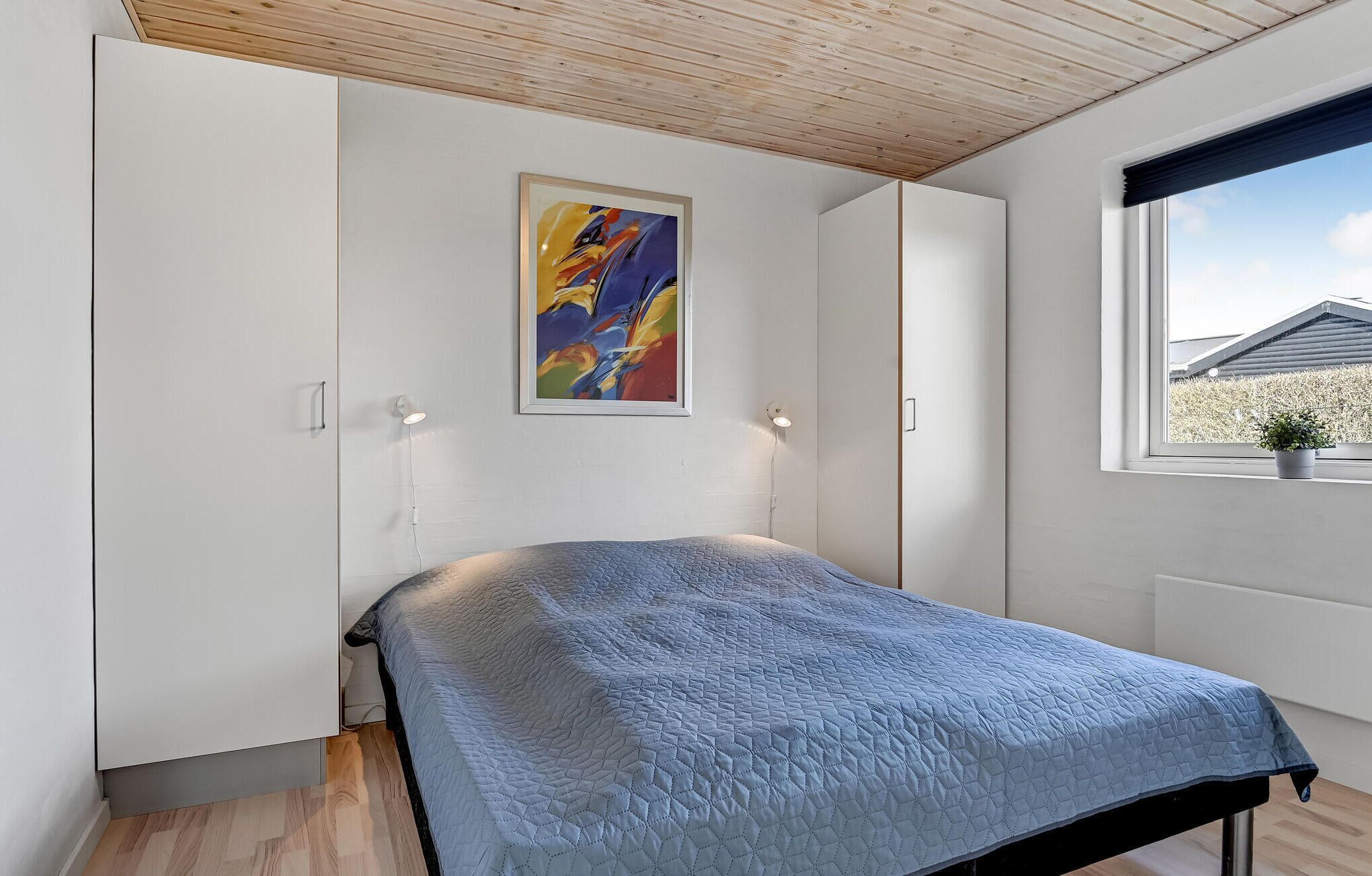 Um quarto com cama, janela com vista e um quadro na parede.