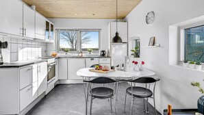 Een moderne keuken met witte kasten, een houten plafond en een groot raam met uitzicht op bomen.