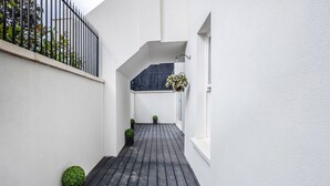 A narrow, wooden-floored corridor with white walls, a black metal fence, and potted plants.