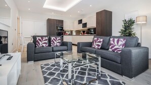A modern living room with two grey sofas, a glass coffee table, and a patterned rug.