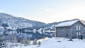 A wooden cabin by a lake with snow-covered surroundings. - Lovely home in Masfjordnes with WiFi (Masfjordnes)