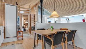 Eine moderne Küche mit Holdekor, ein Essbereich mit Tisch und Stühlen sowie ein Blick ins Freie durch große Fenster.