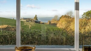 Ein Zimmer mit großen Fenstern, das Blick auf eine grüne Landschaft, ein Gebäude und ein Gewässer bietet.