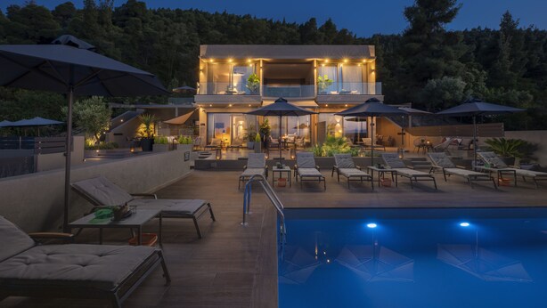 A two-story building with a pool, outdoor seating, and ambient lighting. - Anmian Suites (Sithonia)
