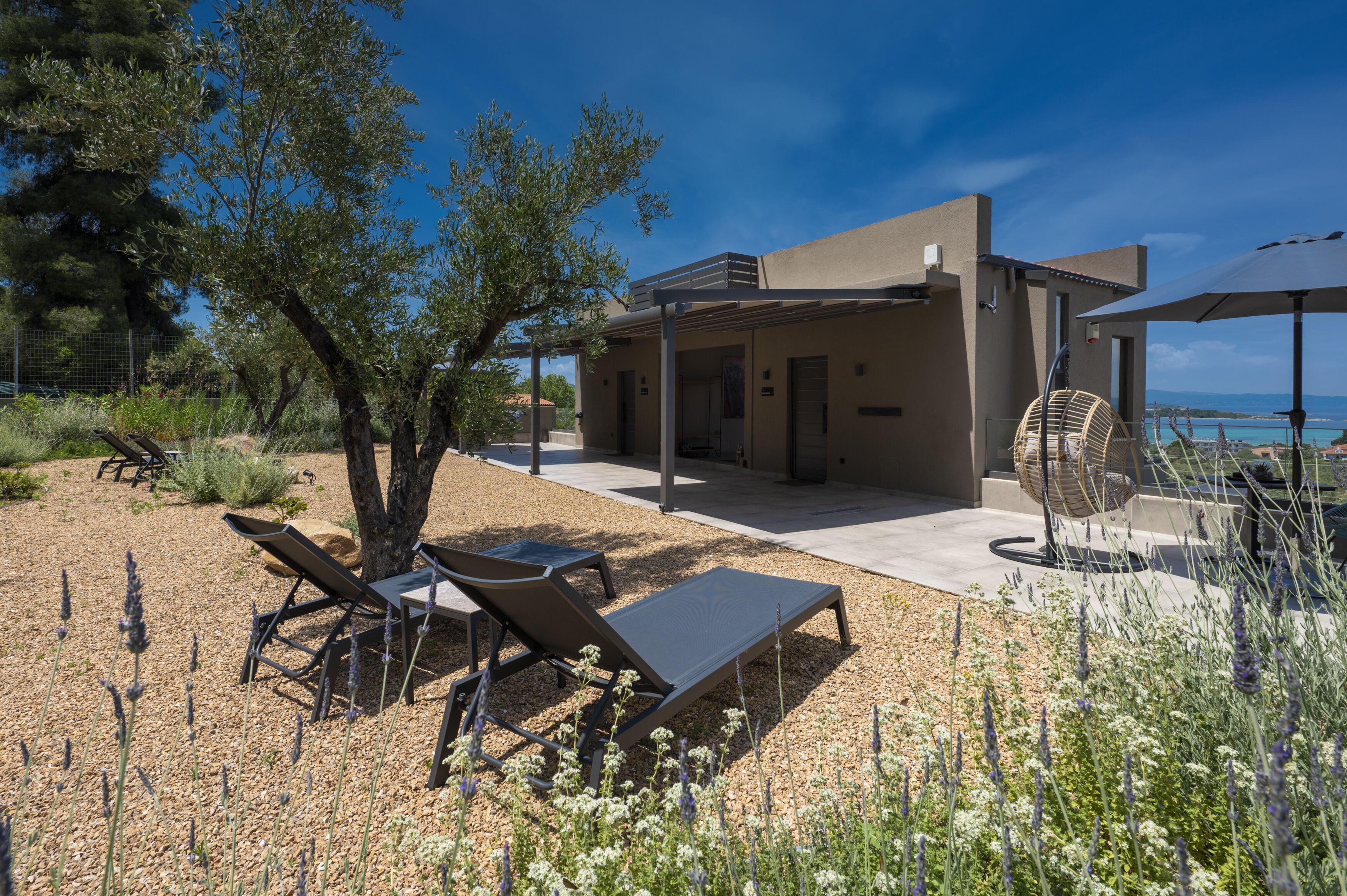 A modern outdoor area with lounge chairs, a fan, and a view of the sea.