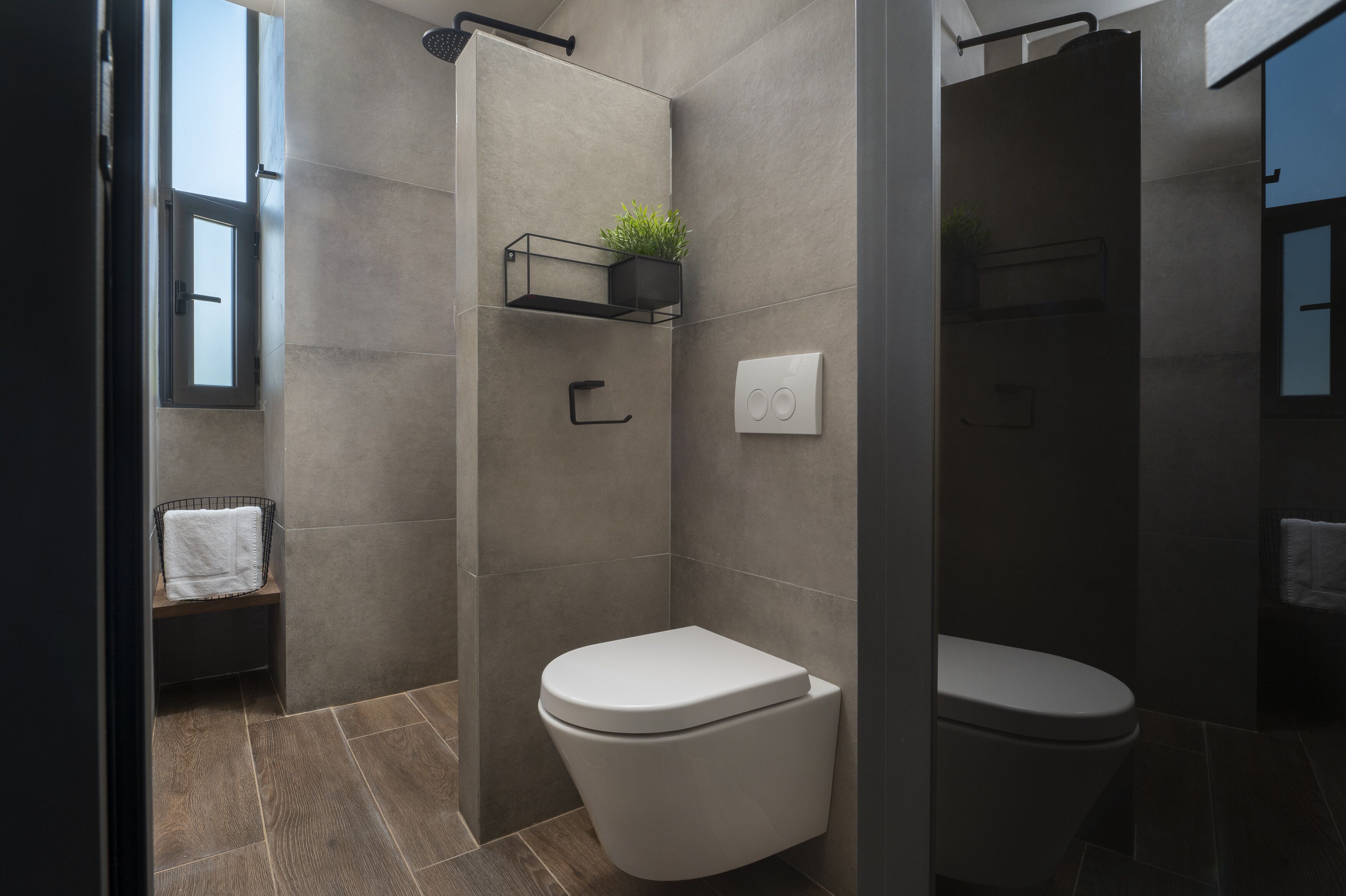Un baño moderno con ducha, inodoro y un pequeño banco con una toalla.