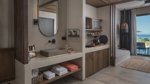 A modern bathroom with a large mirror, a sink, and a vanity with storage. There is a view of the ocean through a large window. - Anmian Suites (Sithonia)