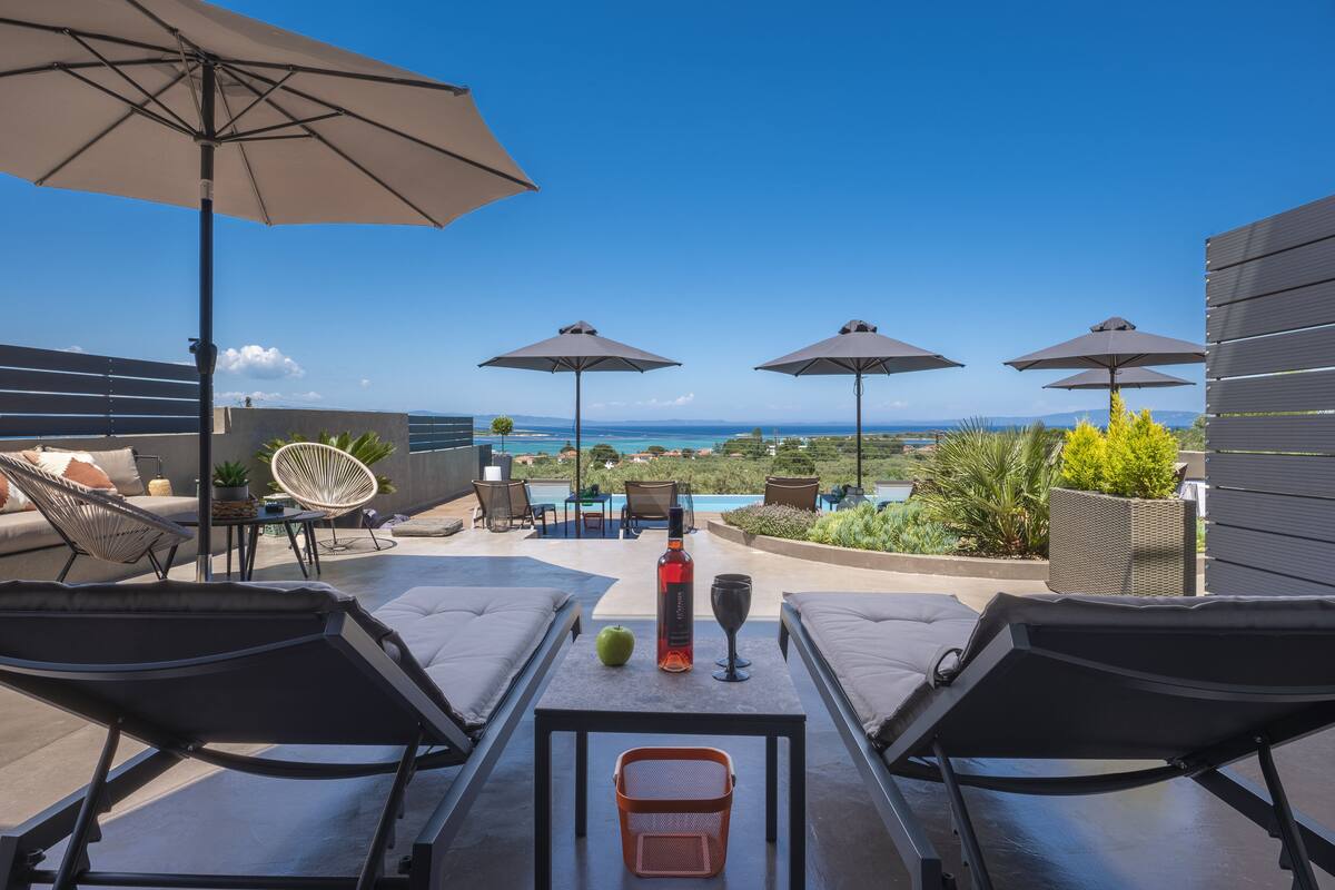 A rooftop terrace with lounge chairs, umbrellas, and a table with a bottle and glass.