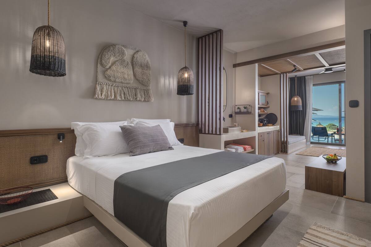 A modern hotel room with a large bed, a desk, and a view of the ocean.