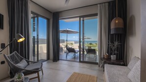 A modern living room with a sofa, a chair, a lamp, and a view of the ocean through large glass doors. - Anmian Suites (Sithonia)