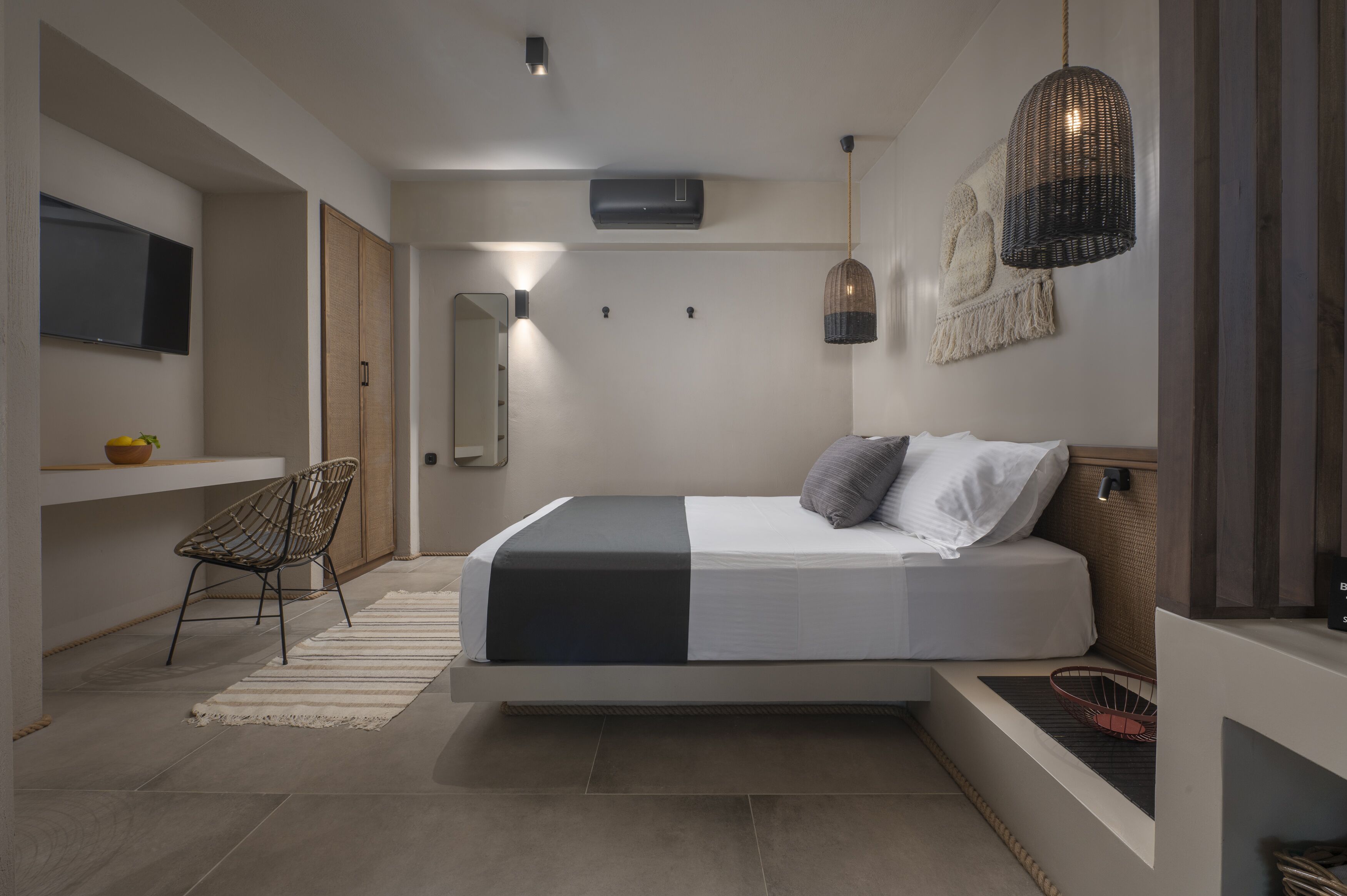 A modern bedroom with a bed, a chair, a TV, and a wall-mounted air conditioner.